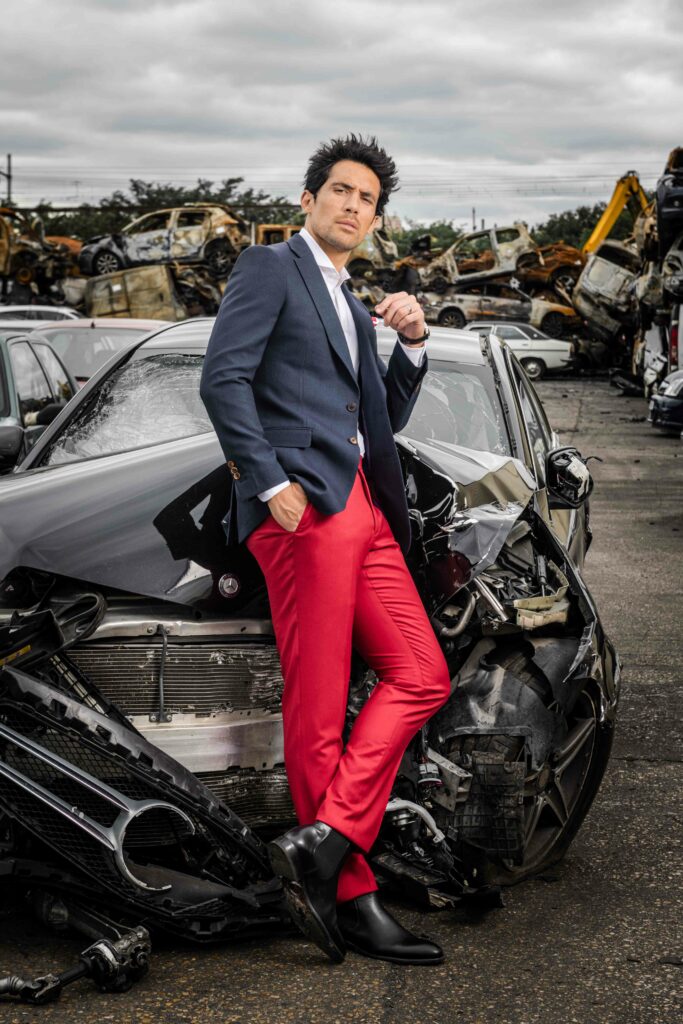 Photo de mode montrant un homme qui se trouve dans une case auto, entouré de pièces de voiture dans son costume de la marque The French Tailor Paris